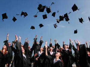 newly graduated people wearing black academy gowns throwing hats up in the air