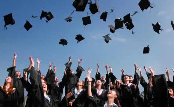 newly graduated people wearing black academy gowns throwing hats up in the air